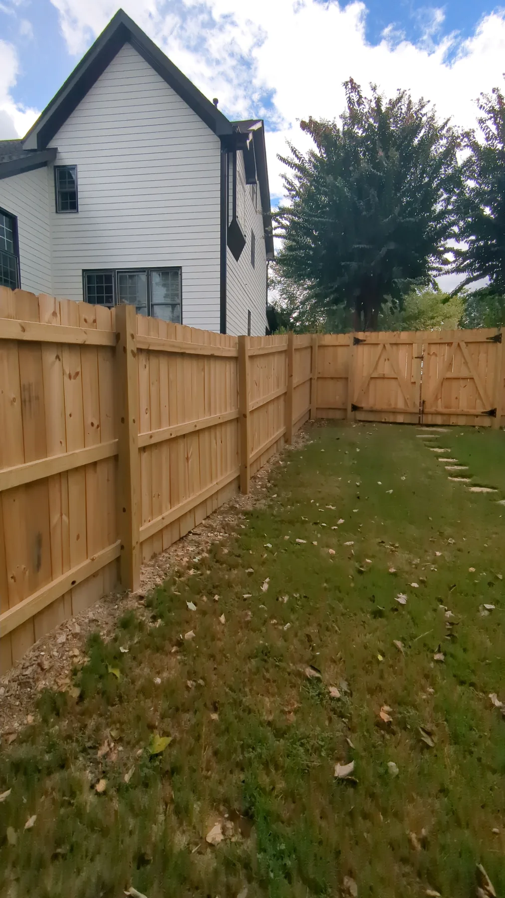 Unfinished wood privacy fence beside a neighboring home