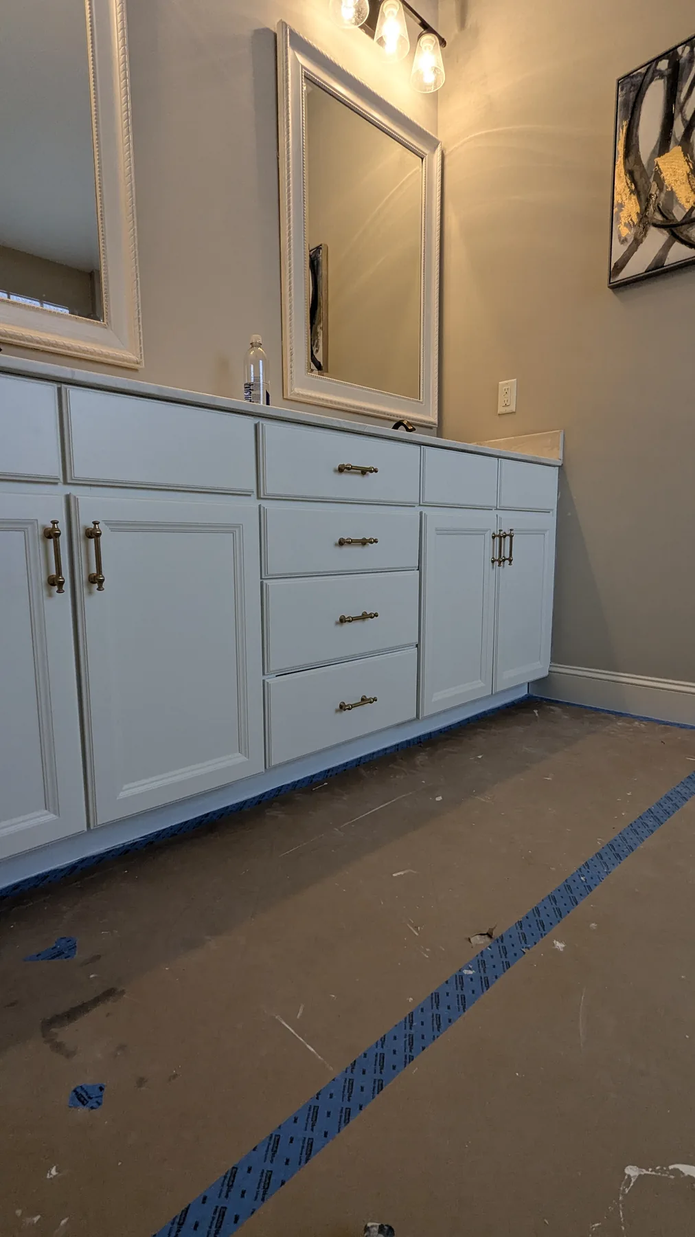 Pale blue painted vanity cabinets with brass handles and protected flooring